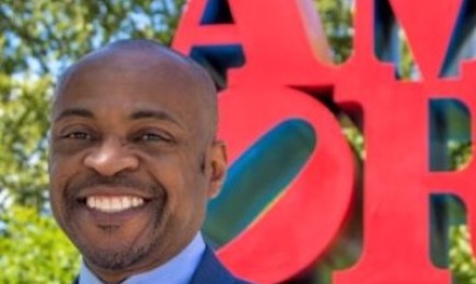 A photo of a person in front of a red sign.