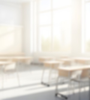 A blurred photo of a sunny classroom with desks and chairs.
